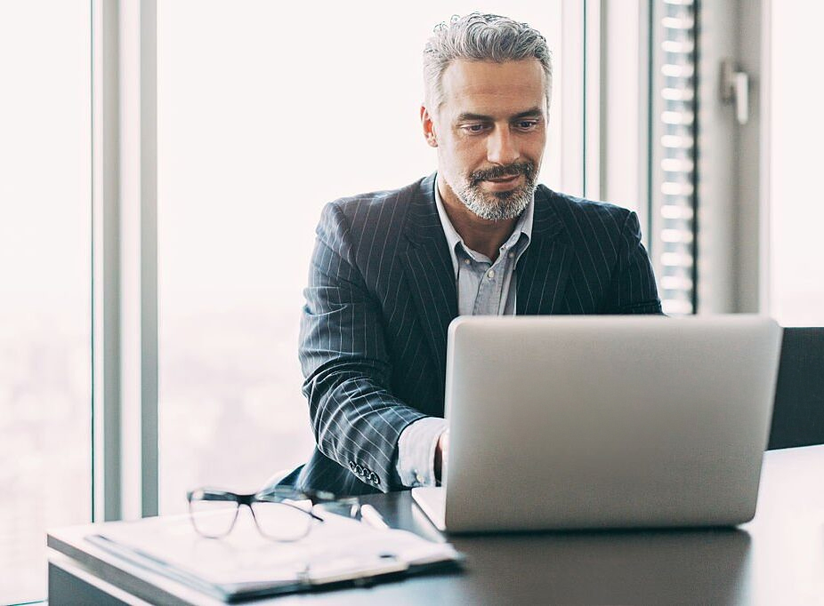 Experienced businessman working on a laptop in a modern office.